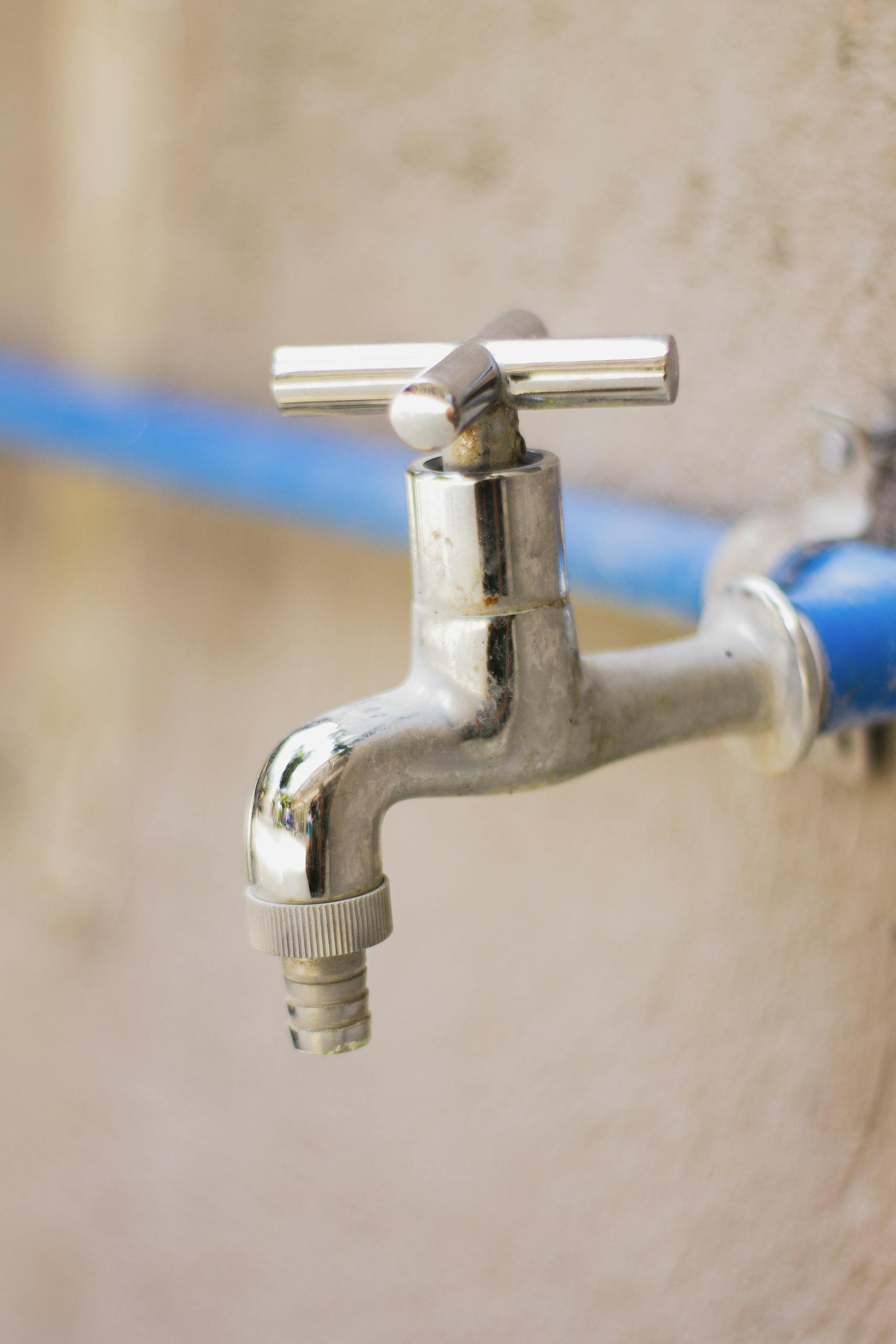 A close-up view of a shiny stainless steel faucet attached to a blue pipe on a wall.