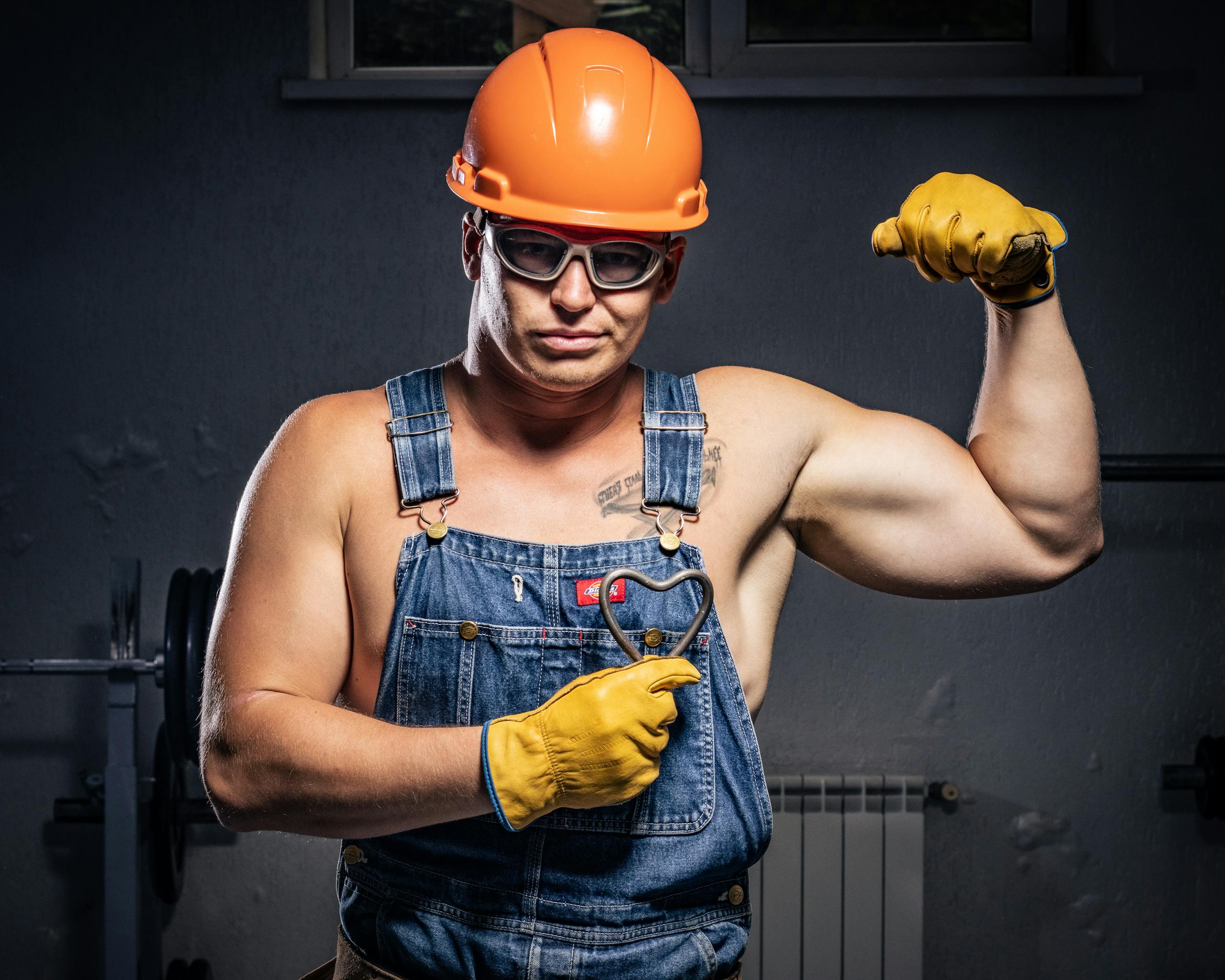 Strong construction worker in denim overalls flexing his muscles with confidence.